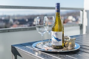 Una botella de vino, dos copas y una bandeja en un balcón con vista a la ciudad.