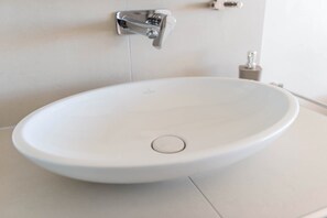 Un lavabo de color blanco con grifo cromado, un dispensador de jabón y un porta toallas de papel en la pared.