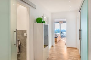 Un couloir avec un plancher en bois, une armoire blanche sur laquelle repose un objet vert, et un lit avec une vue en arrière-plan.