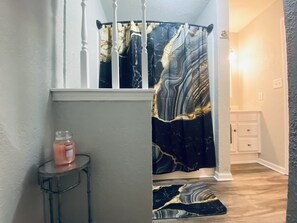 A bathroom with a black and gold marble shower curtain, a small round table with a candle, and a marble-patterned rug on the floor. - 15miles to stadiums-walking distance to local bars (Grain Valley)