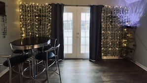 Un coin repas avec une table ronde et quatre chaises, une porte avec des rideaux et un mur décoré de guirlandes lumineuses.