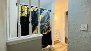 Un couloir avec un rideau à motifs de marbre, une porte blanche et un interrupteur sur le mur.