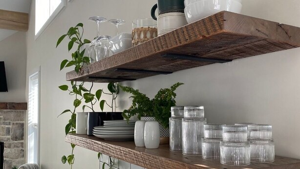 Een keuken met een witte betegelde spatwand, houten planken met glazen en een koffiezetapparaat op het aanrecht.