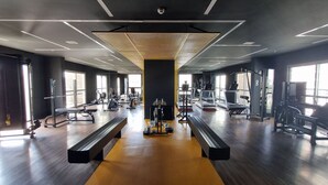Une salle de sport moderne dotée d’un plancher en bois, d’équipements d’exercice et de grandes fenêtres laissant entrer la lumière naturelle.