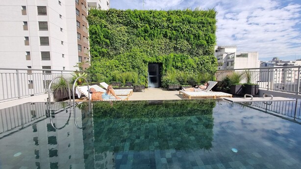 Une piscine à débordement avec des chaises longues et un mur végétal.