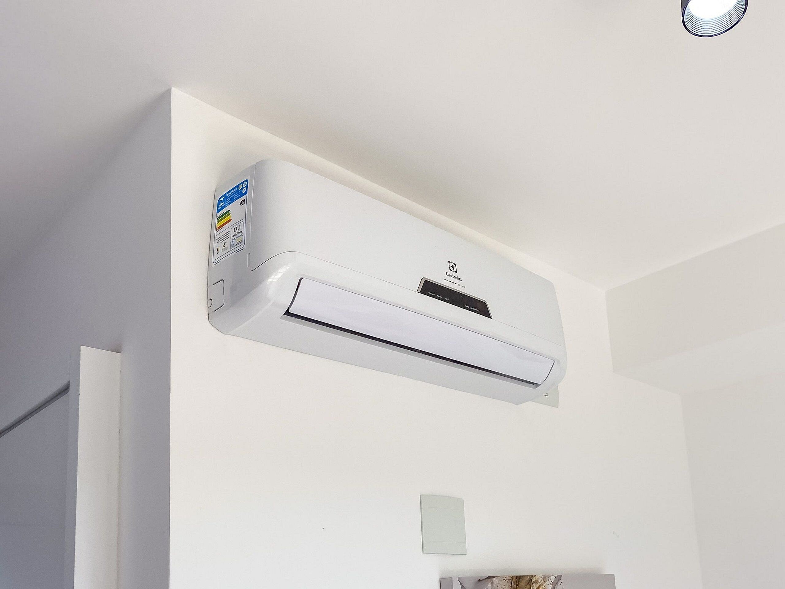 Un equipo de aire acondicionado blanco montado en una pared de una habitación con paredes y una puerta blancos.