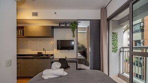 Une chambre d’hôtel moderne, équipée d’un lit, d’un petit bureau, d’une télévision et offrant une vue sur le balcon extérieur.