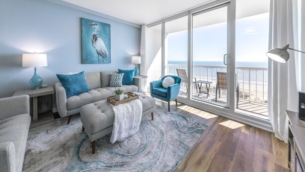 A modern living room with a sofa, armchairs, and a view of the ocean through large windows.