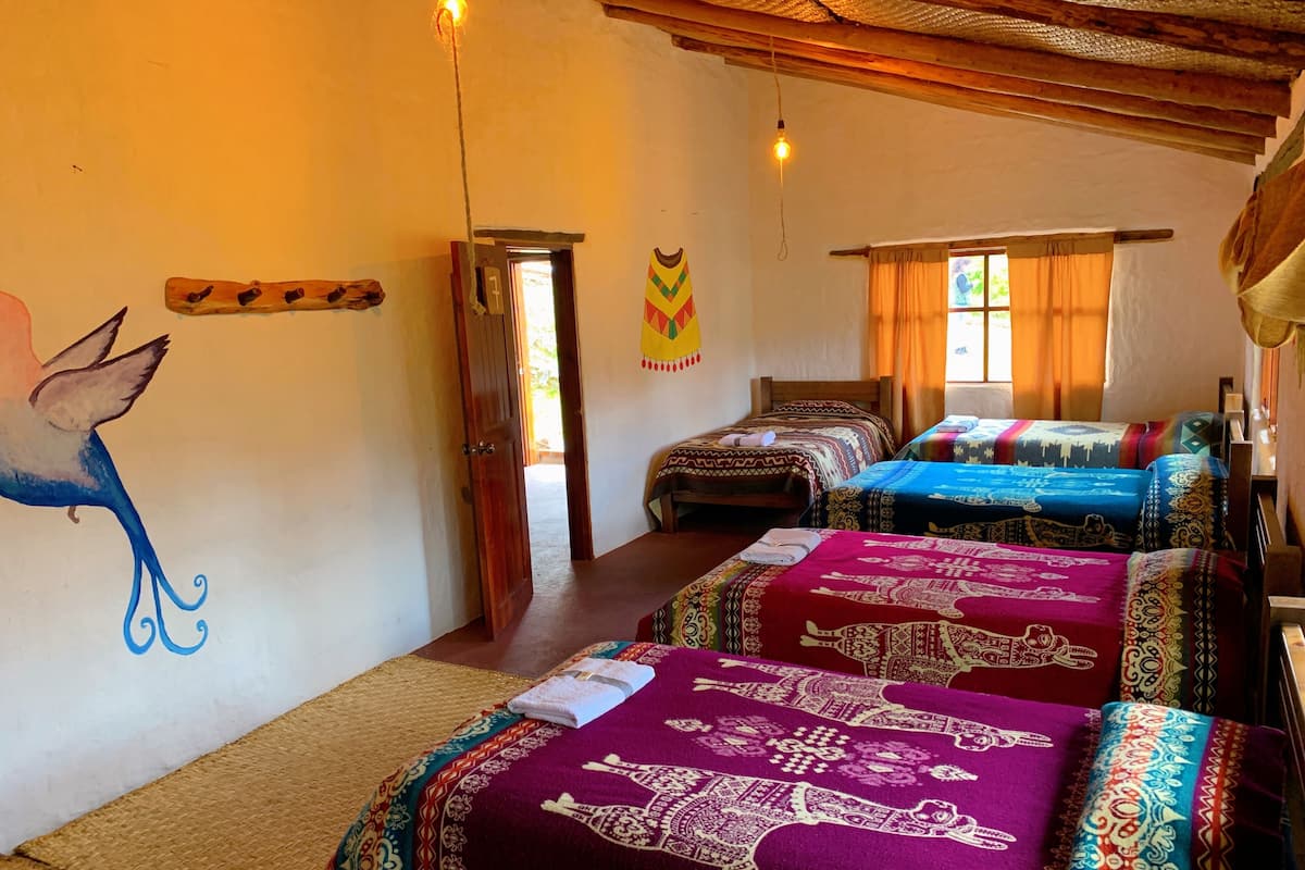 Quarto com três camas, cada uma com roupa de cama estampada, teto de madeira e um mural na parede.