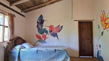 Un dormitorio rústico con techo de madera, una cama con ropa de cama estampada, un mural de pájaros y una puerta.