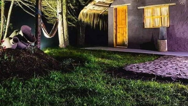 A thatched-roof house with a wooden door and a small porch area, surrounded by lush greenery. - PONDOWASI LODGE (Angochagua)