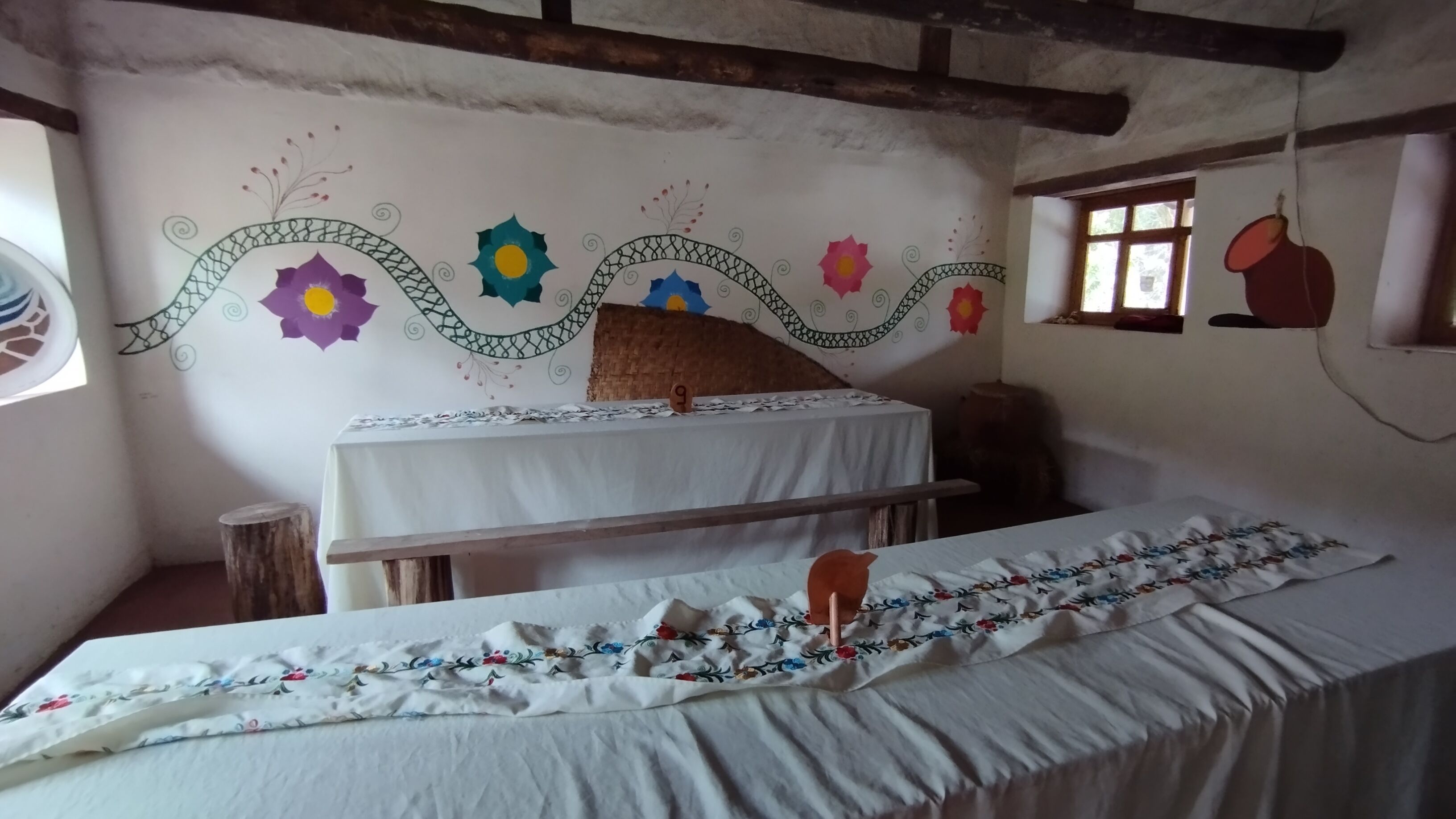 Una habitación con una cama, una mesita pequeña y un muro decorado con motivos florales coloridos.