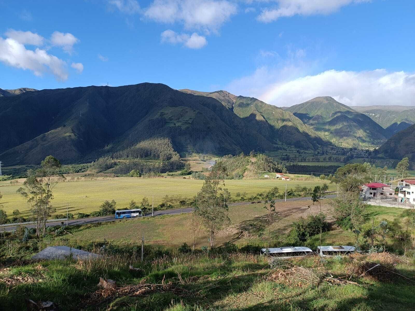 A rural landscape with mountains, a road, and a few buildings.