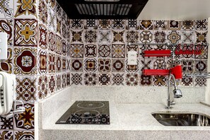 Uma cozinha com painel decorativo atrás do fogão, fogão embutido, pia e torneira vermelha.