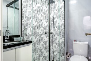 A bathroom with a glass shower enclosure, a toilet, and a sink with a faucet. - Studios delicinha no Brás (São Paulo)