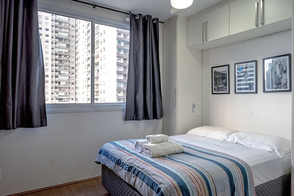 Hotellihuone, jossa on sänky, ikkuna, jossa on verhot, ja seinällä on kehystettyjä kuvia.