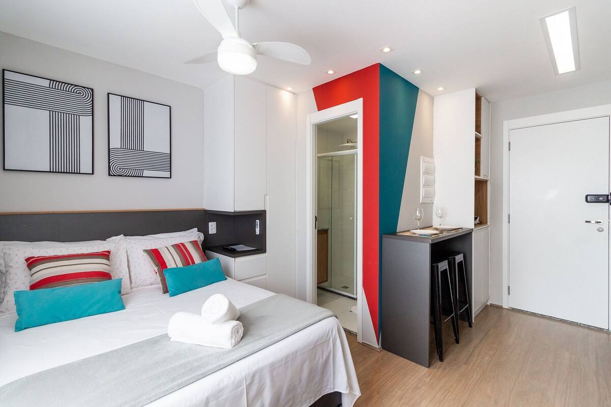 A modern hotel room with a bed, a desk, and a shower area.