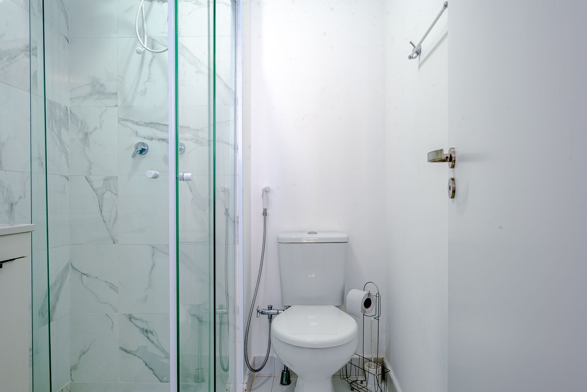Een badkamer met een douche met glazen wand, een wit toilet en een handdoekrek.