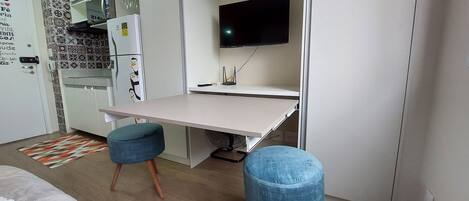 Une petite cuisine équipée comprenant un four à micro-ondes, un réfrigérateur et une petite table à manger avec deux tabourets bleus.