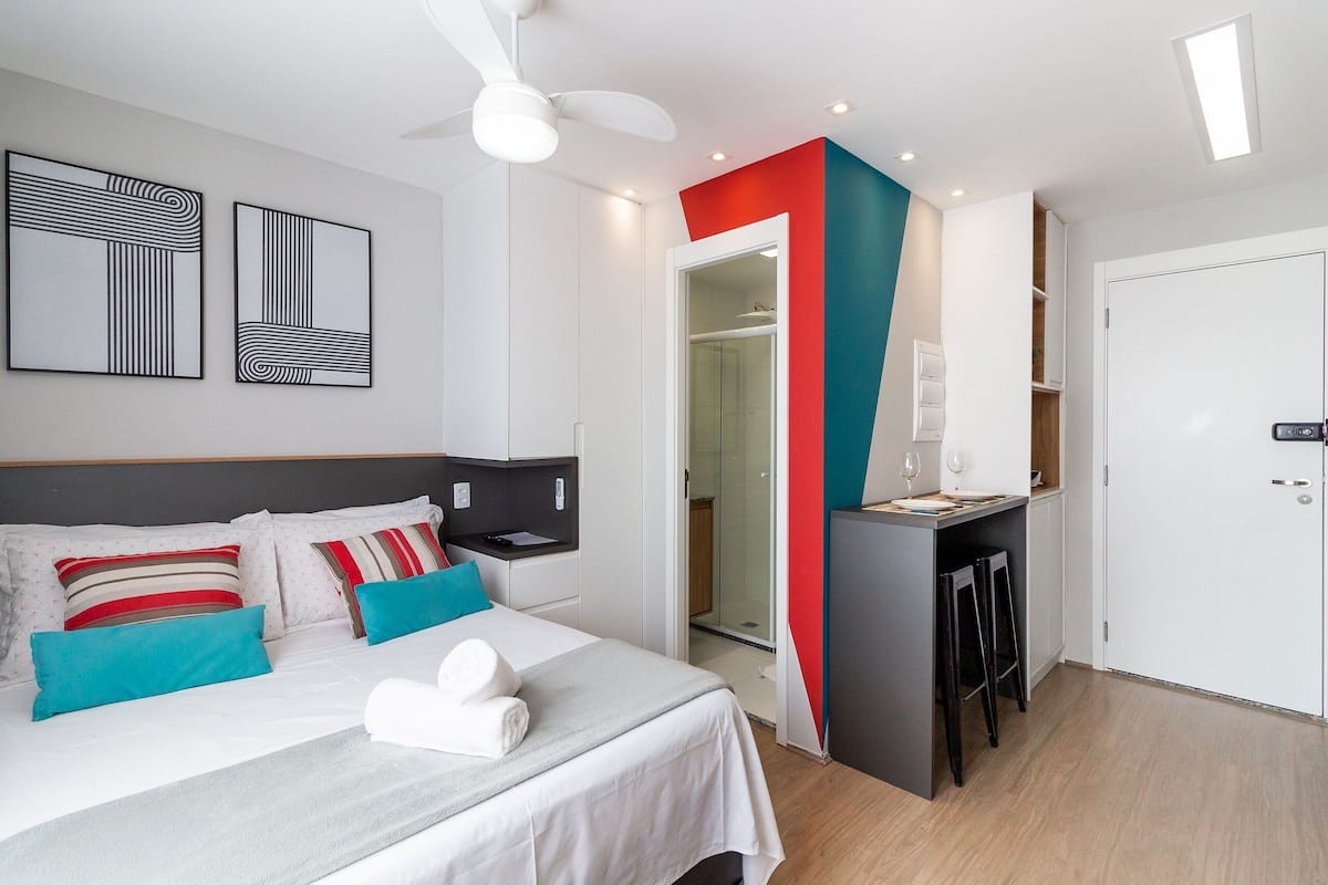 Moderni hotellihuone, jossa on sänky, työpöytä ja suihkutila.