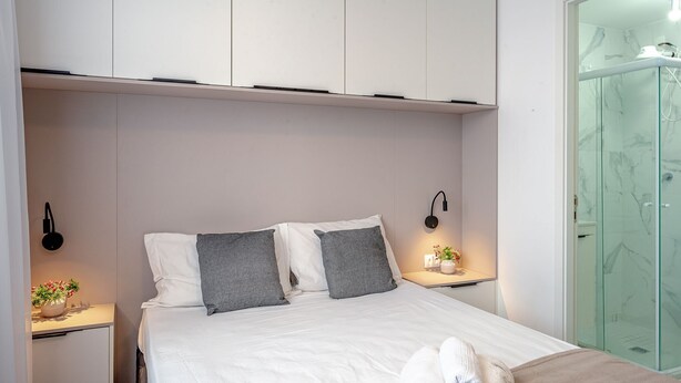 A modern bedroom with a bed, bedside tables, and a glass shower enclosure.