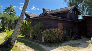 Una casa de madera con techo inclinado, rodeada de palmeras y arbustos.