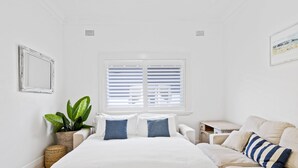 Ein Schlafzimmer mit Bett, Nachttisch, Lampe, Topfpflanze und einem Fenster mit Jalousien.
