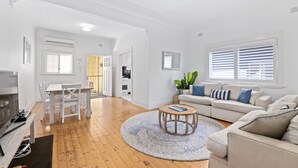 Ein geräumiges Wohnzimmer mit Holzboden, einem runden Couchtisch, einem weißen Sofa und einem Essbereich mit weißem Tisch und Stühlen.