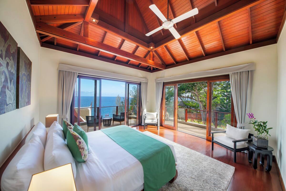 A spacious bedroom with a large bed, a ceiling fan, and a view of the ocean through large sliding doors.