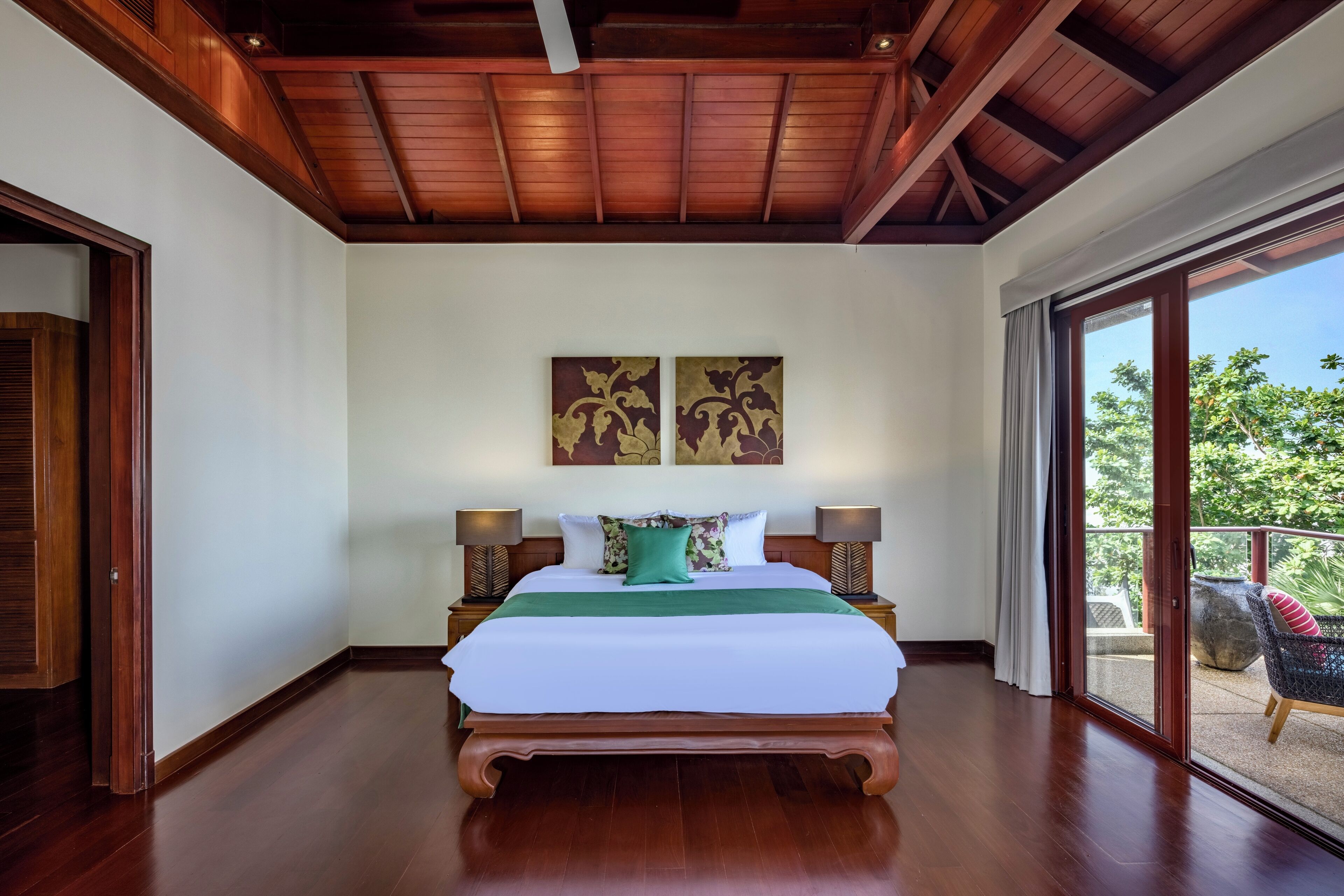 A spacious bedroom with a large bed, wooden ceiling, and a balcony with a view of greenery.