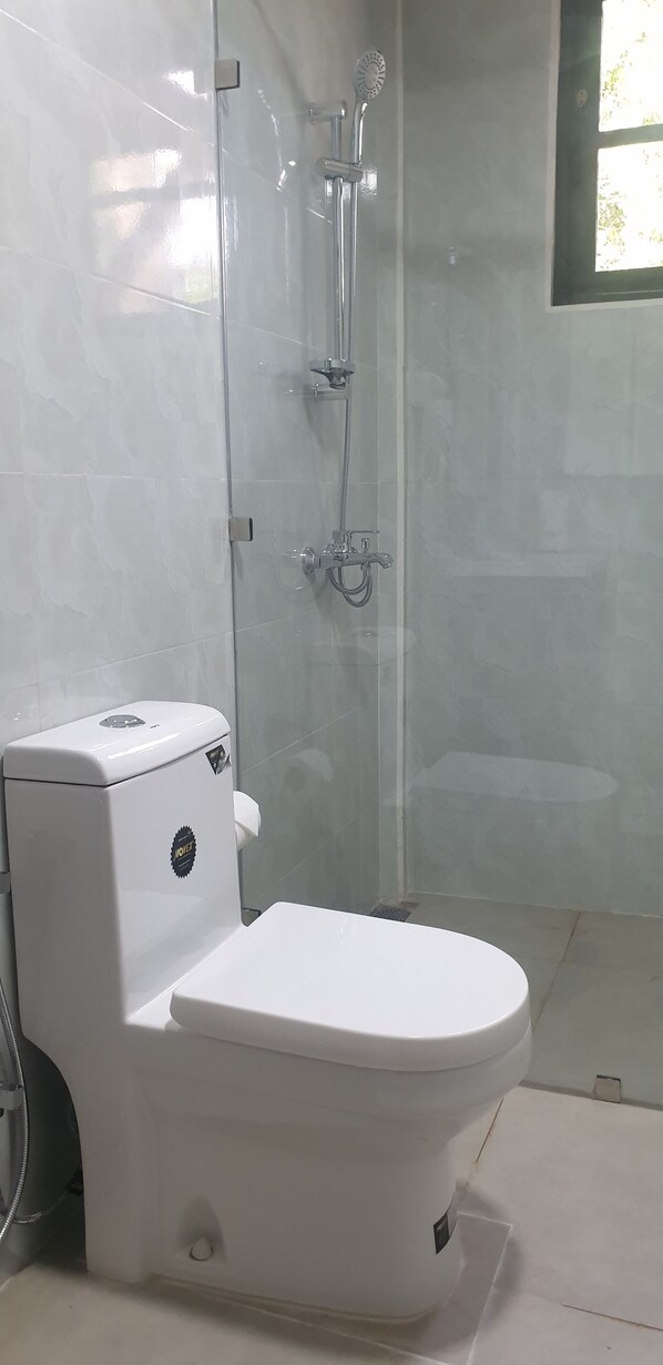 A bathroom with a toilet, a glass-enclosed shower, and a window.