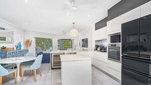 A modern kitchen with white cabinetry, a black refrigerator, and a dining area with a round table and chairs. - Coral Horizons Beachfront Apartment (Cairns)