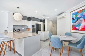 Une cuisine moderne dotée d’un îlot central, de meubles blancs et d’un coin repas avec des chaises bleues.