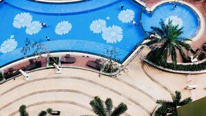 A large pool with a flower design, surrounded by lounge areas and palm trees. - Kelly House at Vinhomes Central Park (Ho Chi Minh City)