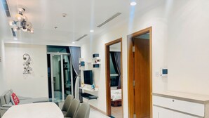 A modern hotel room with a dining area, a bed with a TV, and a wooden door. - Kelly House at Vinhomes Central Park (Ho Chi Minh City)