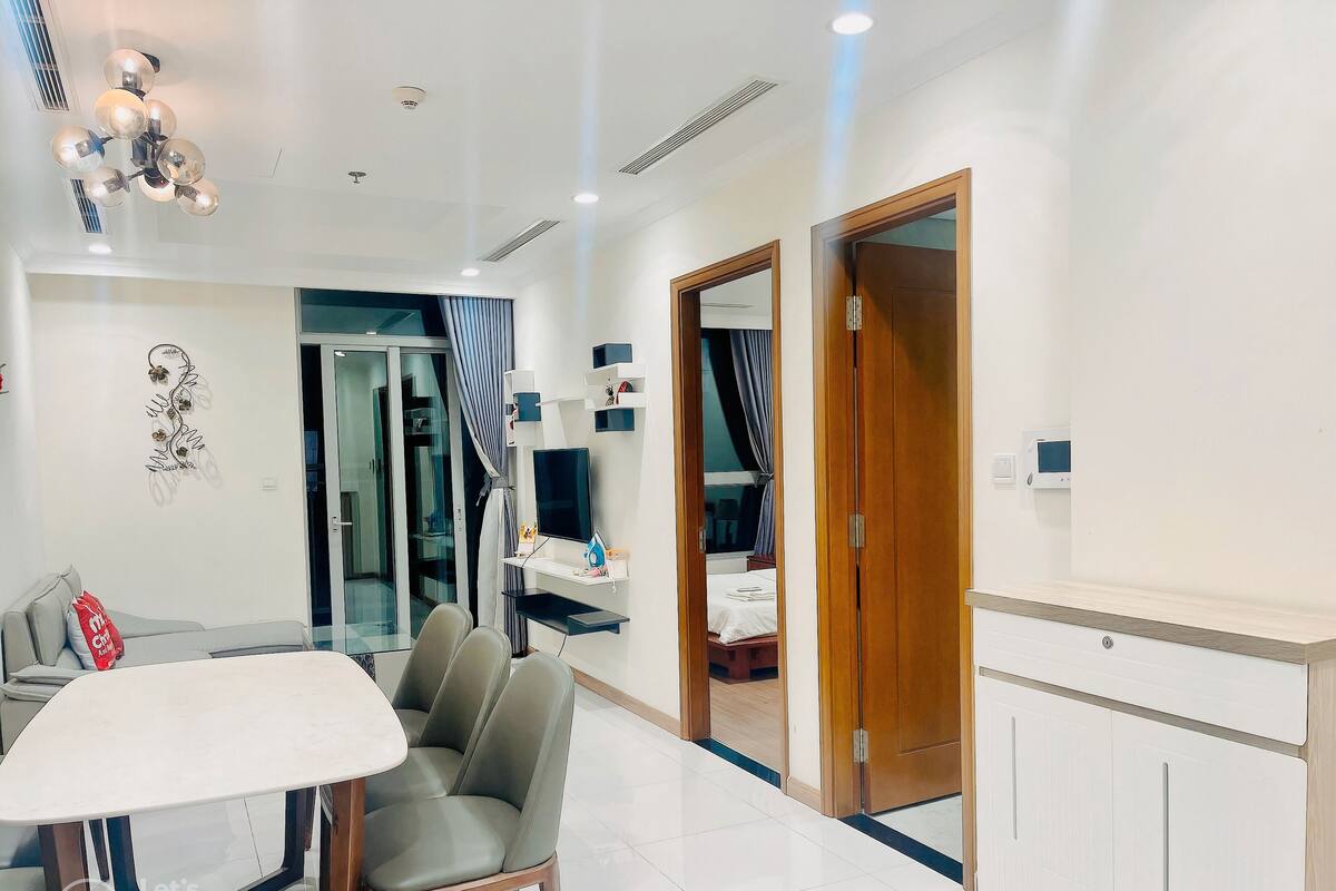 A modern hotel room with a dining area, a bed with a TV, and a wooden door.