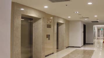 Corredor moderno com elevadores, um extintor de incêndio e uma placa indicando que o edifício é um apartamento urbano.
