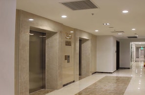 A modern hallway with elevators, a fire extinguisher, and a sign indicating the building is a City Apartment. - Kelly House at Vinhomes Central Park (Ho Chi Minh City)