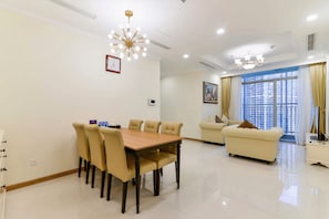 Uma sala de estar moderna com área de jantar, apresentando uma mesa de jantar de madeira, sofás bege e uma grande janela com vista para a cidade.