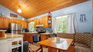 A compact kitchen with wooden cabinets, a stainless steel refrigerator, and a dining area with a wooden table and patterned sofa. - Lakeview cabin, 3 min walk to the beach! (Grand Marais)