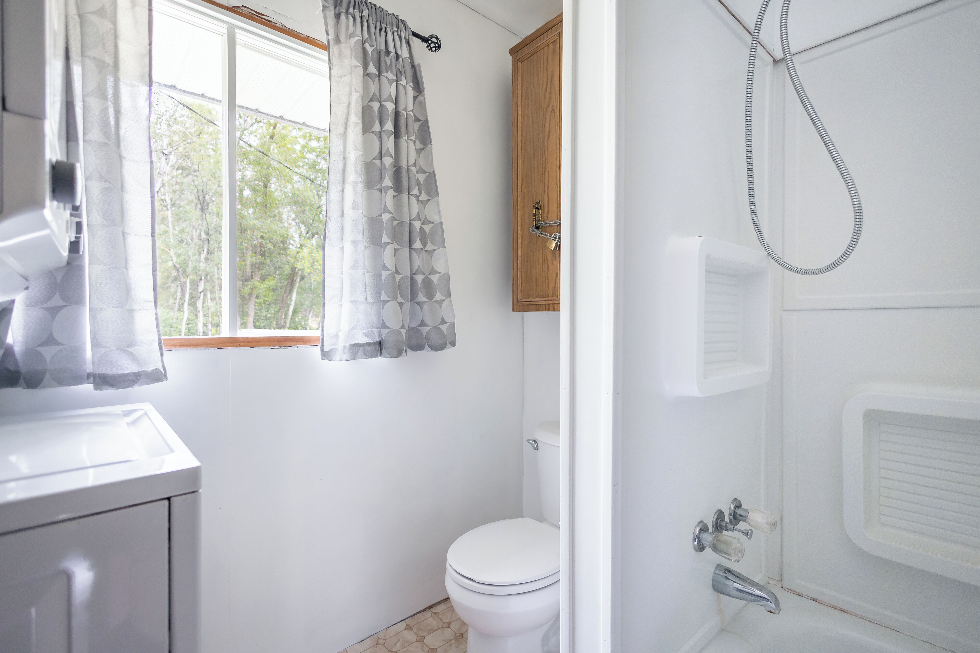 A bathroom with a toilet, a shower, and a window with a curtain.