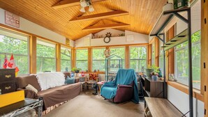 A cozy cabin interior with a wooden ceiling, large windows, a couch, a chair, and a small table. - Lakeview cabin, 3 min walk to the beach! (Grand Marais)