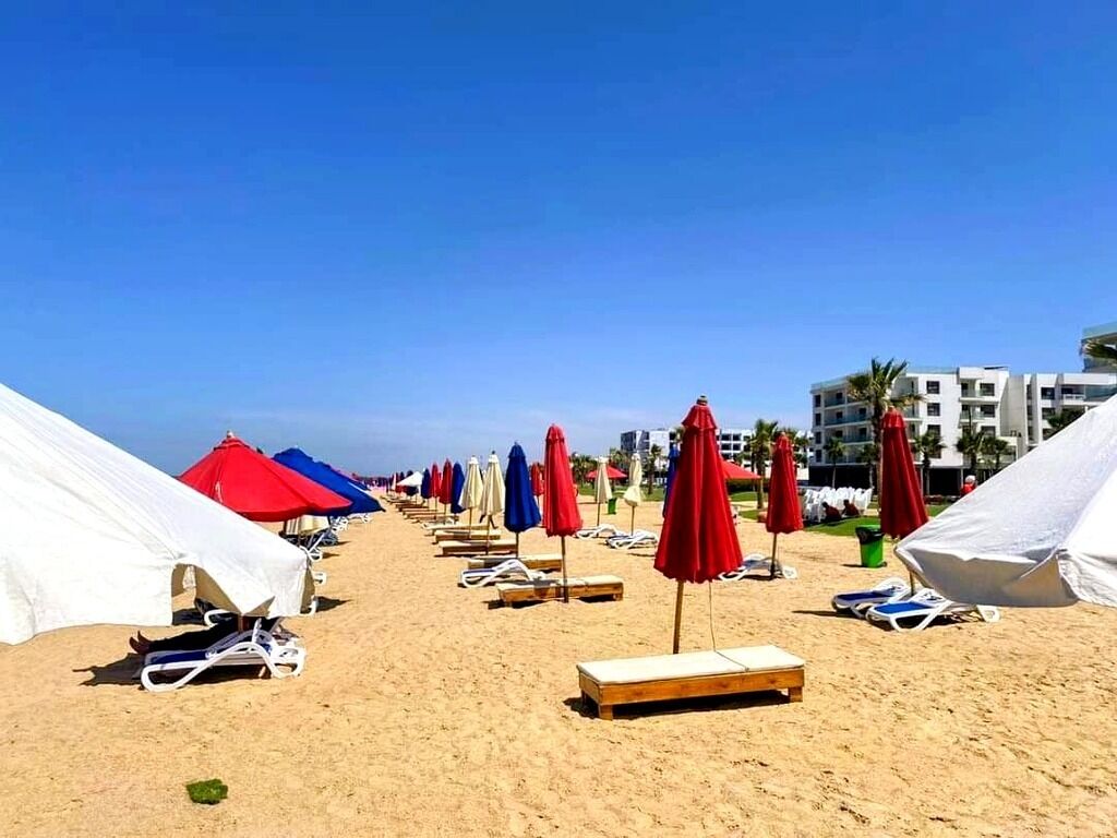 A beach with rows of sun loungers and umbrellas, some covered by white canopies.
