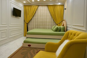 Une chambre à coucher de taille modeste, avec un lit, un fauteuil jaune et un téléviseur fixé au mur.