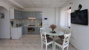 Une cuisine moderne avec un coin repas, des meubles blancs et un téléviseur à écran plat fixé au mur.
