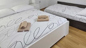 Une chambre avec deux lits, chacun doté d’un matelas blanc et de motifs abstraits noirs, un plancher en bois et une table de chevet blanche avec une lampe.