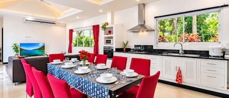 A modern dining area with a table set for six, red chairs, and a kitchen with white cabinets and a large window.