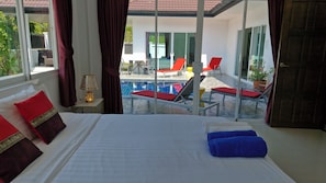 A hotel room with a bed, a view of a pool area, and a sliding glass door. - Phikun Private Pool Villa (Chalong)