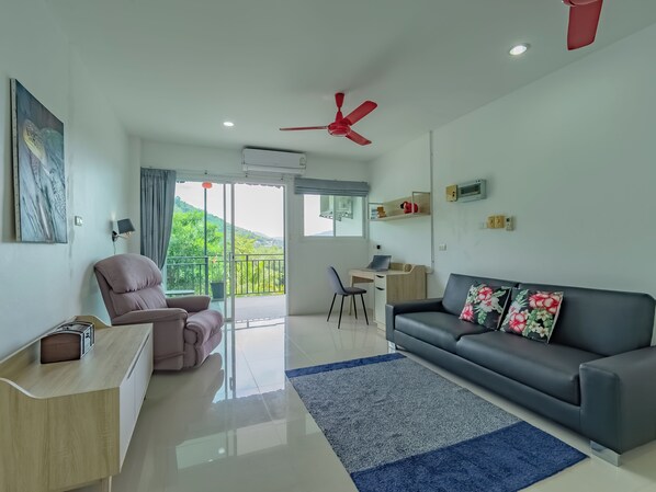 Un salon moderne comprenant un canapé, un bureau, une chaise et un balcon avec vue sur la verdure.