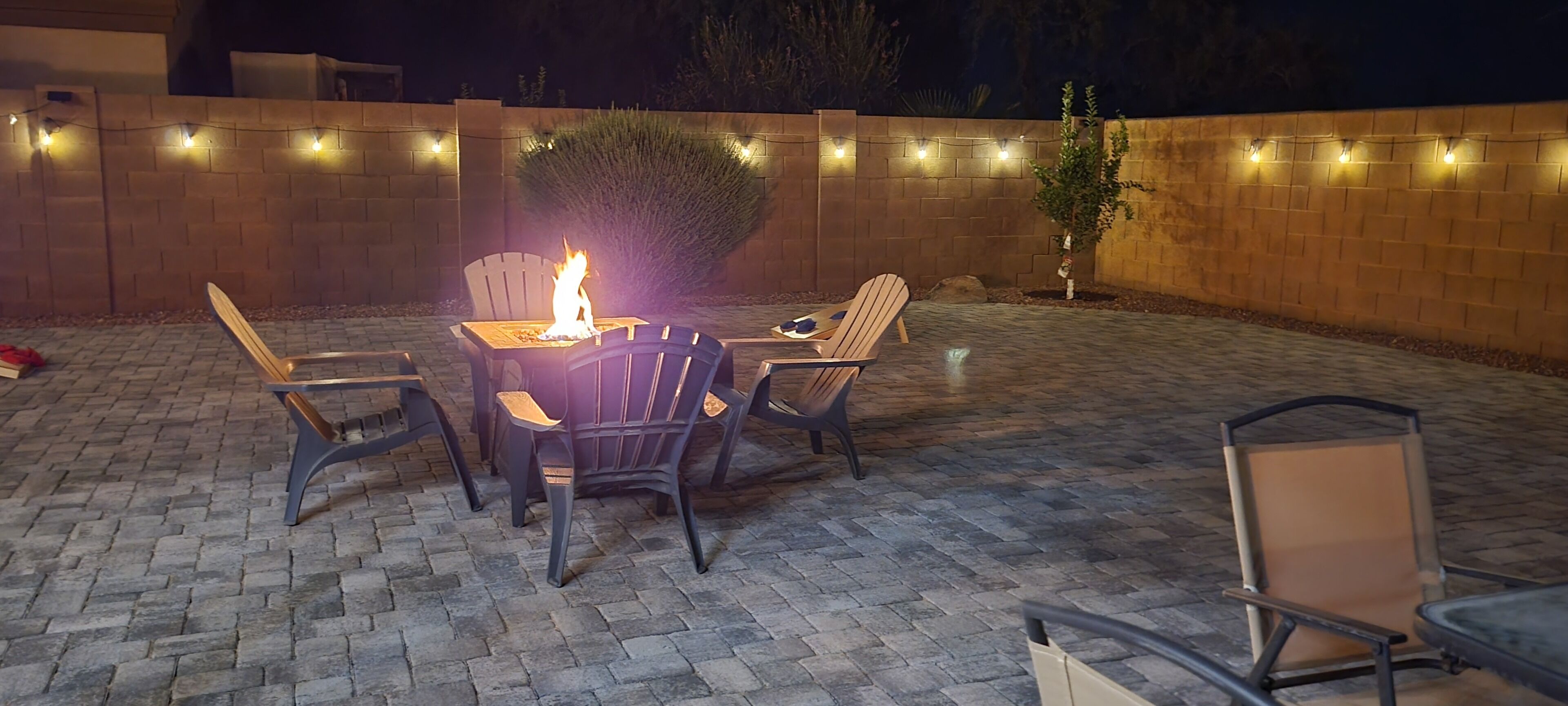 An outdoor patio with a fire feature, seating, and string lights.